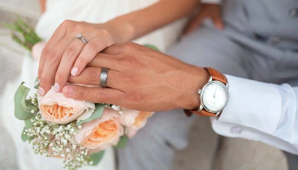 newly weds hands with weddings rings on top of the brides wedding bouquet