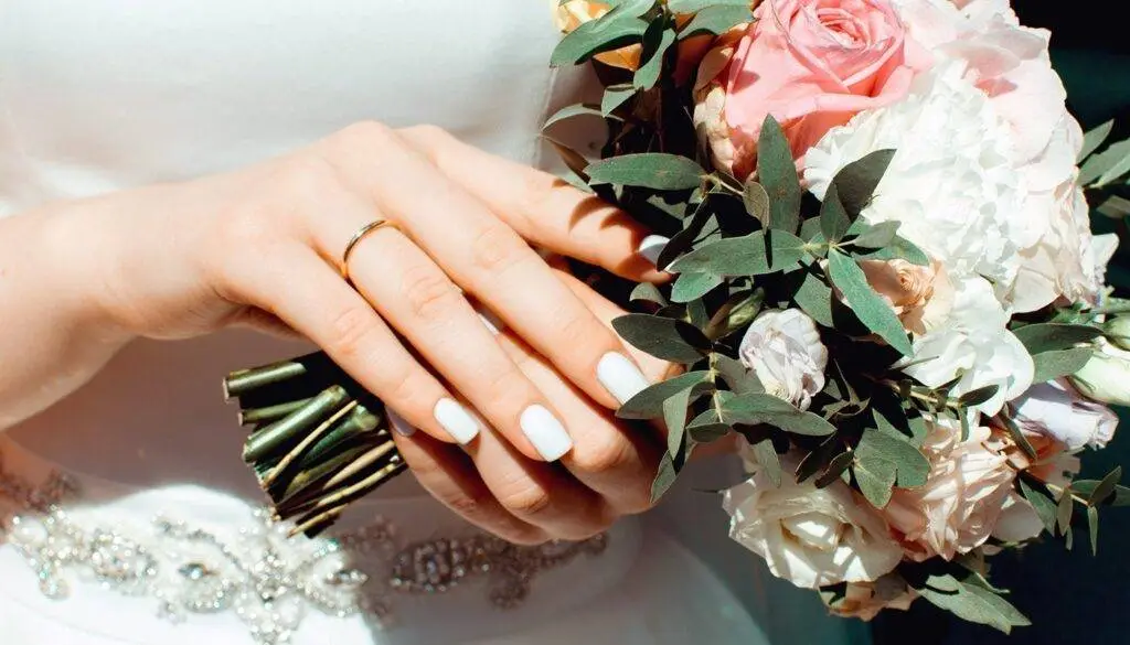 brides hand with her wedding ring holding her wedding bouquet