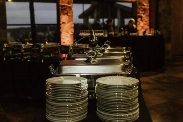 warm ambience long tables with silver food warmers and dinner plates each with golden decorative lining