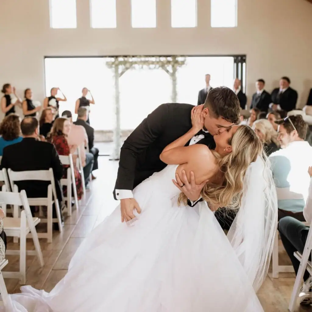 A couple shares a romantic kiss at the altar in El Cerrito’s elegant indoor venue, surrounded by guests and a joyful wedding atmosphere.